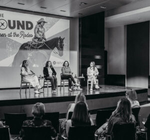 Four women seated on stage in a fireside chat format at Optura's In The Round: Women at the Rodeo event, with an audience of women in the foreground.
